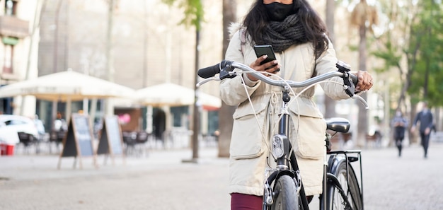 Photo photo panoramique d'une jeune femme afro-américaine méconnaissable à l'aide d'un téléphone intelligent sur son vélo. elle est dans une ville.