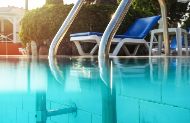 Photo partiellement sous-marine, mains courantes en acier à l'entrée de la piscine, soleil à contre-jour brillant en arrière-plan. Image vacances / détente.