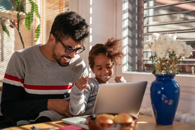 Photo d'un père et d'une fille américains jouant sur un ordinateur à l'intérieur