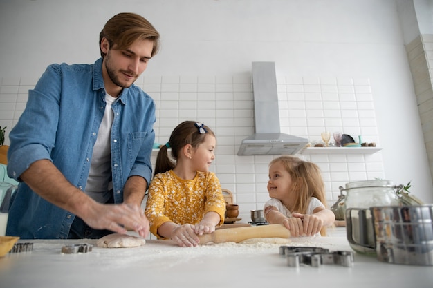 Photo d'un père et de ses filles souriants qui cuisent dans la cuisine et s'amusent.