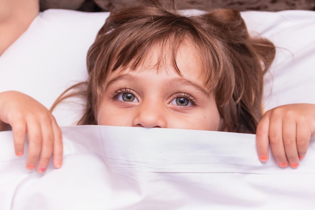 Photo d'un petit enfant caucasien couché dans son lit avec un drap sur le visage ne montrant que les yeux