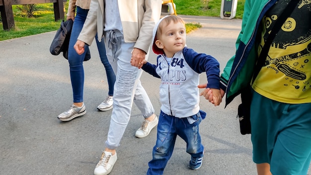 Photo d'un petit garçon tenant sa mère et son frère aîné à la main et marchant dans un parc en automne