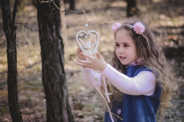 Photo d'une petite fille aux cheveux longs dans un bandeau rose jouant dans la forêt