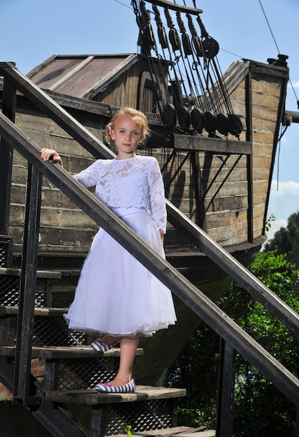 Photo d'une petite fille en robe blanche pose sur un vieux bateau en bois