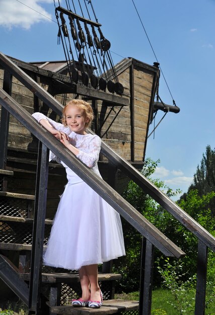 Photo d'une petite fille en robe blanche pose sur un vieux bateau en bois