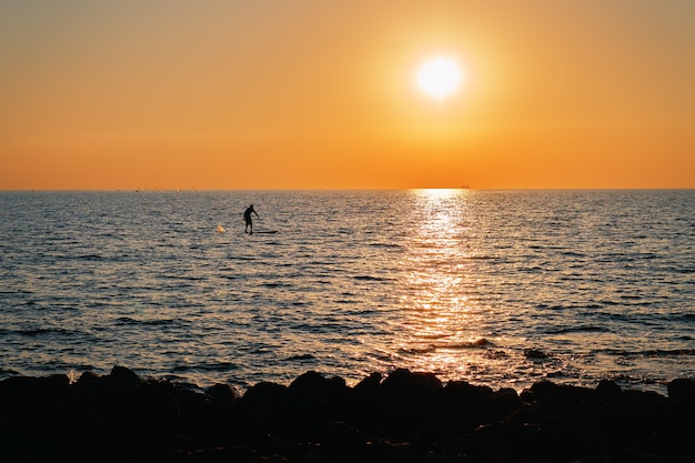 Photo avec une petite silhouette d'un surfeur méconnaissable dans la belle mer sans limites au coucher du soleil. Mode de vie sain et actif