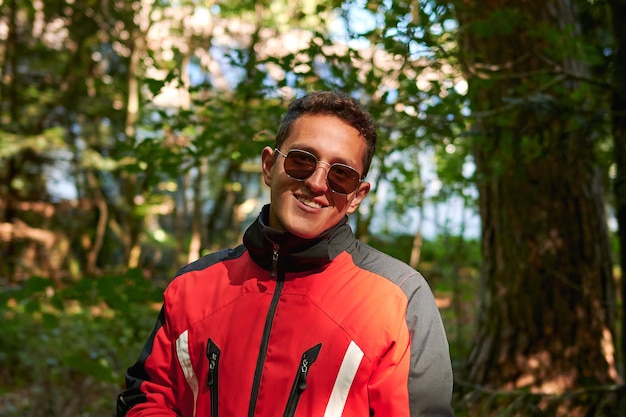 Une photo peu profonde d'un beau jeune homme hispanique avec des lunettes de soleil et un manteau souriant dans la nature