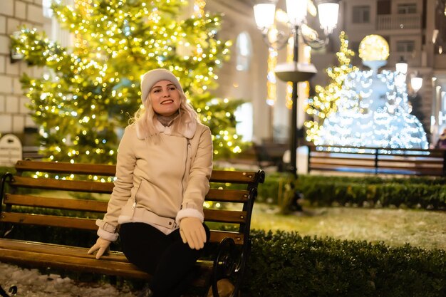 Photo en plein air de la belle jeune fille souriante heureuse tenant des cierges magiques, posant dans la rue. Foire de Noël festive sur fond. Modèle portant un manteau d'hiver élégant, un bonnet tricoté, une écharpe.