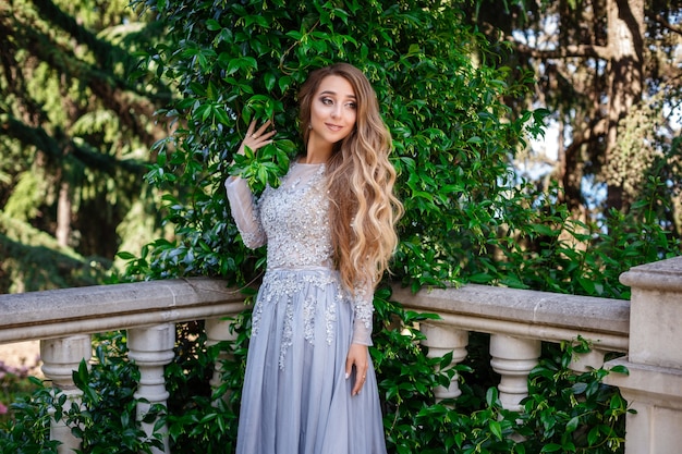 Photo en plein air de mode d'élégante belle femme aux cheveux blonds en robe de paillettes luxueuses et accessoires en argent, posant dans le parc d'été