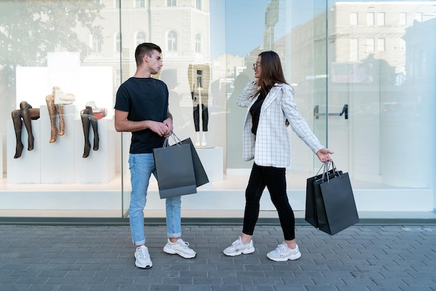 Photo pleine grandeur couple d'amis avec des sacs à provisions sur fond de vitrine vendredi noir