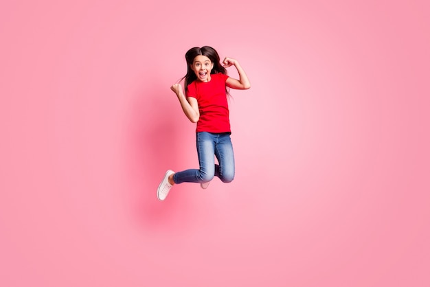 Photo pleine grandeur d'une fille ravie qui saute le poing en portant une tenue de style décontracté isolée sur fond de couleur rose