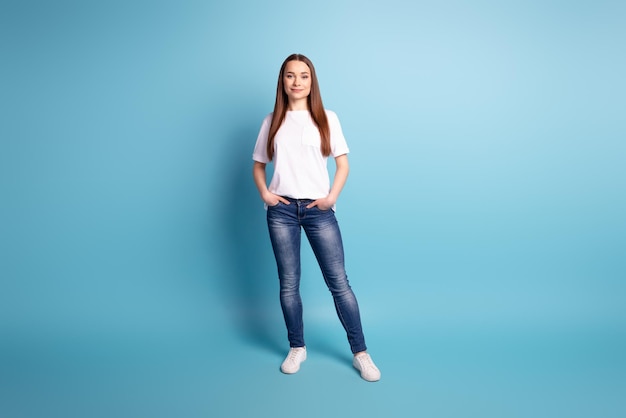 Photo pleine grandeur d'une jeune fille attarctive de bonne humeur bras dans la poche confiante isolée sur fond de couleur bleue