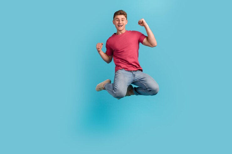 Photo pleine grandeur d'un jeune homme excité sauter les poings mains se réjouir victoire triomphe isolé sur fond de couleur bleue