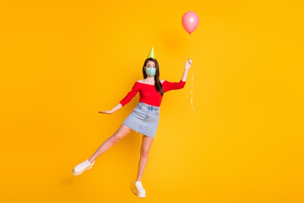 Photo pleine longueur d'une belle fille dans un masque médical attraper un ballon à vent à la volée porter des jambes de jupe en jean décontractées en jean haut rouge isolées sur fond de couleur brillant brillant