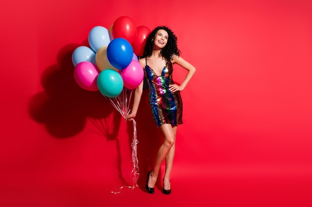 Photo pleine longueur d'une charmante dame tenir des ballons look espace vide porter une mini robe brillante talons hauts isolé fond de couleur rouge vif