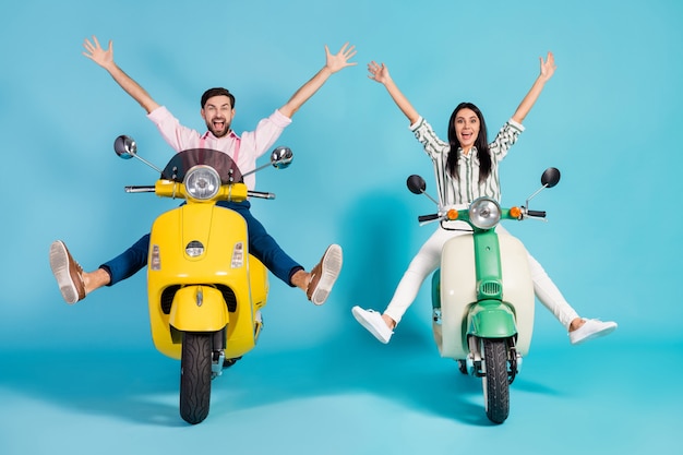 Photo pleine longueur de deux personnes funky lady guy conduire rétro cyclomoteur bonne humeur temps écarté les jambes près de la flaque d'eau lever les bras vêtements de cérémonie fou isolé mur de couleur bleu