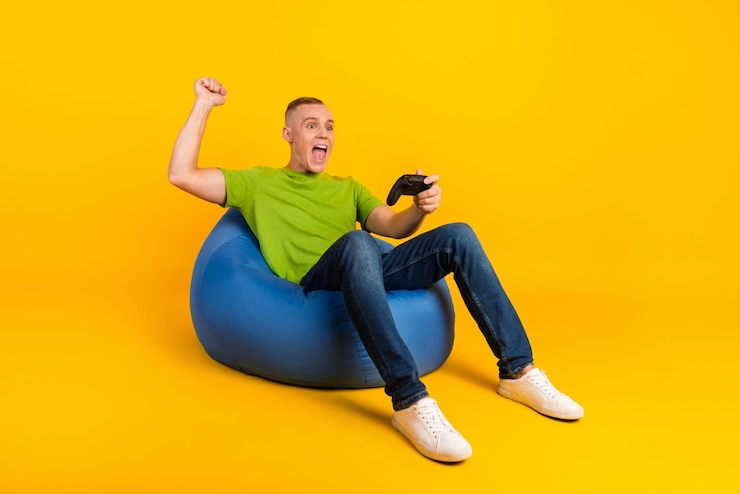 Photo photo pleine longueur d'un drôle d'homme impressionné assis pouf playstation fond de couleur jaune isolé