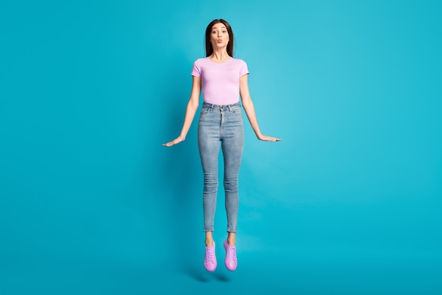 Photo pleine longueur de drôle de jeune fille sauter envoyer un baiser d'air porter un t-shirt rose chaussures jeans isolé fond de couleur bleu