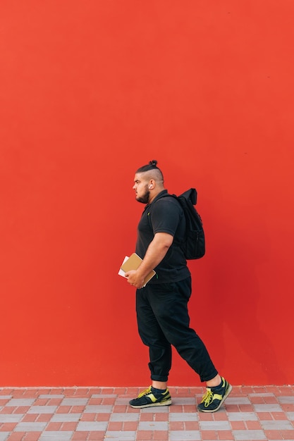 Photo pleine longueur d'un élégant jeune homme en surpoids marchant sur un fond de mur rouge