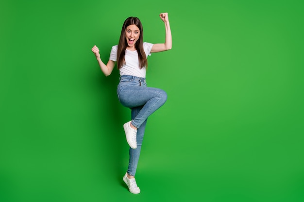 Photo pleine longueur d'une fille gagnante gaie vêtue d'une tenue décontractée, les bras en l'air, bouche ouverte, fond de couleur verte isolé