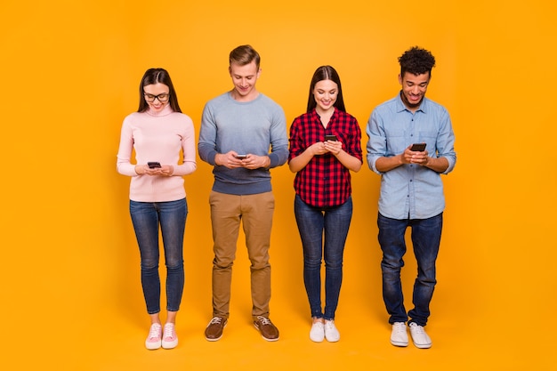 Photo pleine longueur d'un groupe d'amis avec leurs téléphones isolés sur orange