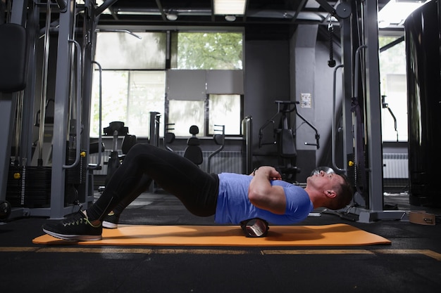 Photo pleine longueur d'un homme de fitness se relaxant après l'entraînement à l'aide d'un rouleau en mousse sur les muscles de son dos