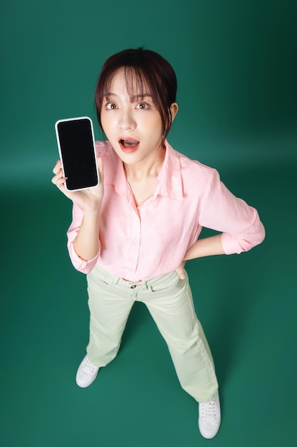 Photo pleine longueur d'une jeune fille asiatique utilisant un smartphone sur fond vert