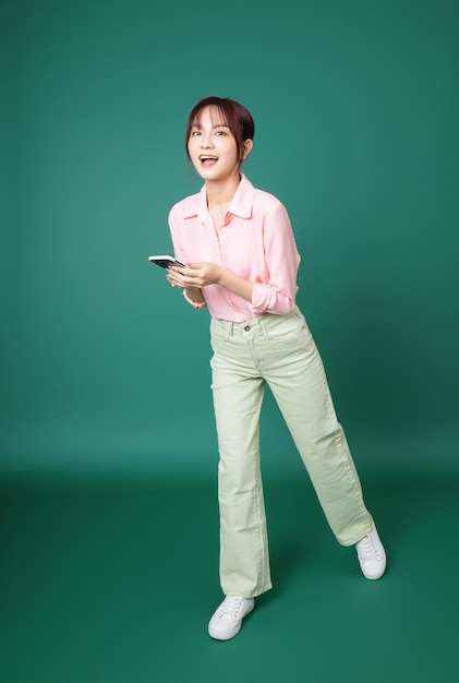 Photo pleine longueur d'une jeune fille asiatique utilisant un smartphone sur fond vert