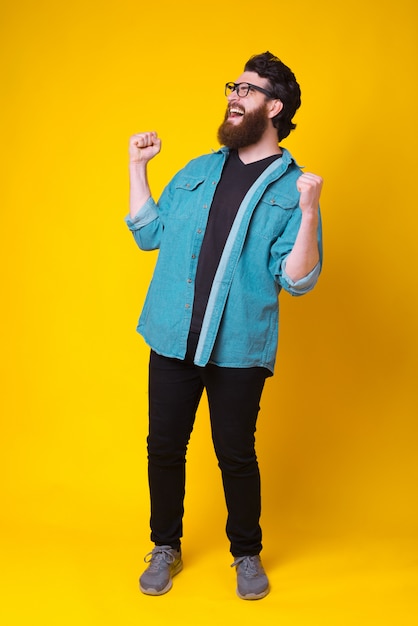 Photo pleine longueur d'un jeune homme étonné avec une barbe célébrant la victoire