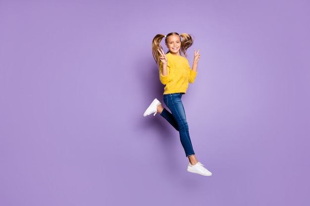 Photo pleine longueur de joyeux saut enfant positif s'amuser pendant les vacances d'automne faire v-signes porter des vêtements de style décontracté isolés sur un mur de couleur violette