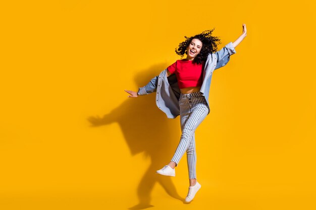 Photo pleine longueur de lady jump lever les mains de jambe porter des jeans rayés recadrée t-shirt rouge veste baskets isolé fond de couleur jaune