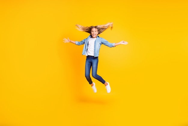 Photo pleine longueur de la taille du corps d'une petite fille souriante et satisfaite aux cheveux longs sautant joyeusement isolé sur fond de couleur jaune vif