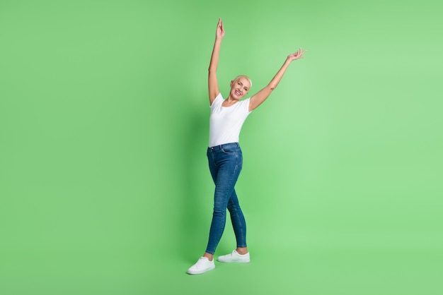 Photo pleine taille d'une femme mature séduisante, les bras levés, portez une tenue décontractée isolée sur fond de couleur verte.