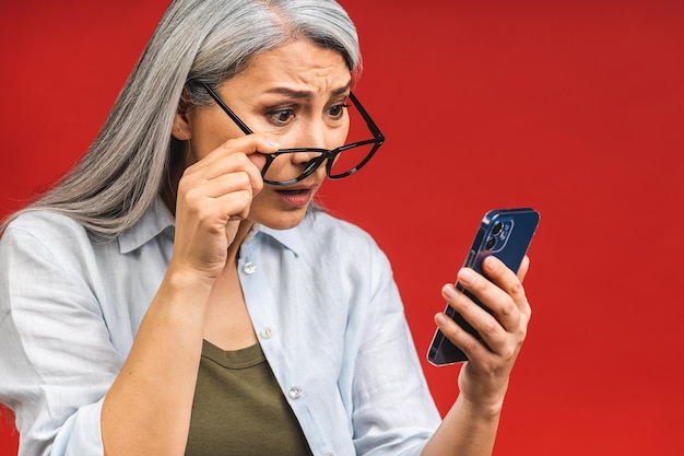 Photo portrait d'une asiatique choquée étonnée surprise d'une femme mûre d'âge mûr tenant un téléphone portable voyant des réductions folles portant des vêtements décontractés isolés sur fond rouge