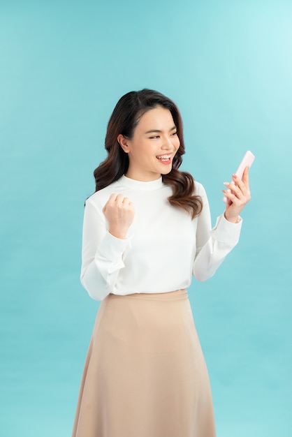 Photo de portrait d'une belle jeune femme asiatique se sentant heureuse ou choquée par surprise et tenant un téléphone intelligent