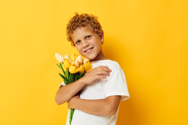 Photo portrait bouclé petit garçon tenant un bouquet de fleurs un cadeau fond jaune inaltéré