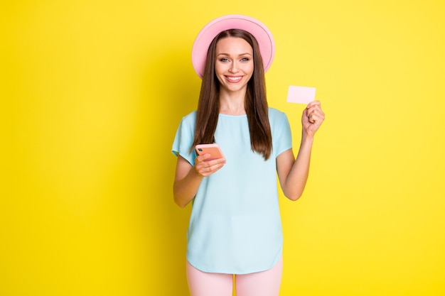 Photo positive fille suivre l'achat de médias sociaux utiliser smartphone payer crédit carte bancaire porter t-shirt bleu rose chapeau de soleil pantalon pantalon isolé sur fond de couleur brillant brillant