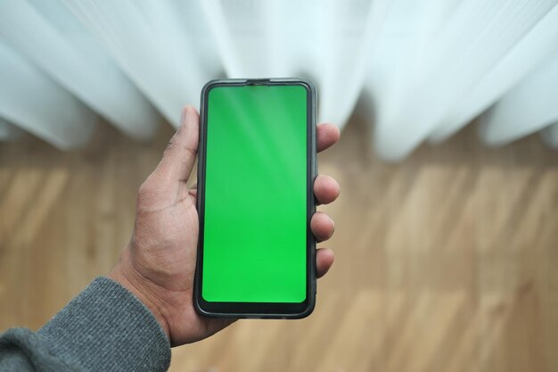 Photo POV d'une main de jeune homme tenant un téléphone intelligent à la maison