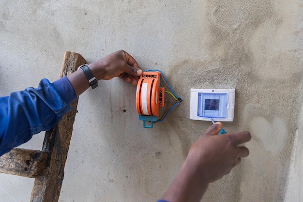 Une photo en premier plan d'un électricien sur une échelle ouvrant une boîte sur le mur