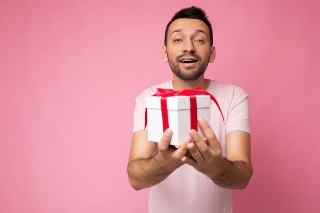 Photo prise de beau positif heureux gentil brune jeune homme mal rasé avec barbe isolé sur rose