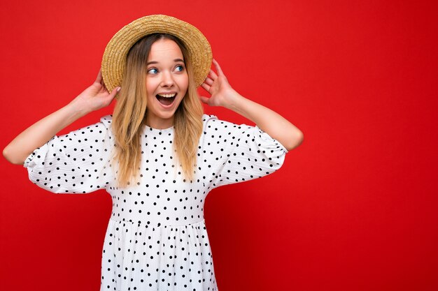 Photo prise de jeune belle femme blonde heureuse mignonne portant une robe décontractée et un chapeau de paille