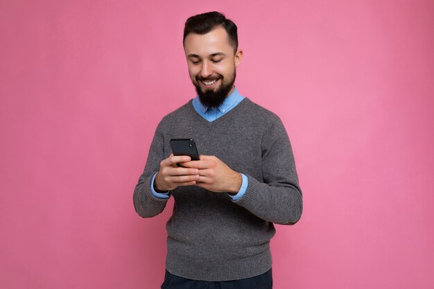 Photo prise de sourire cool beau jeune homme non rasé brunet avec barbe portant un pull gris