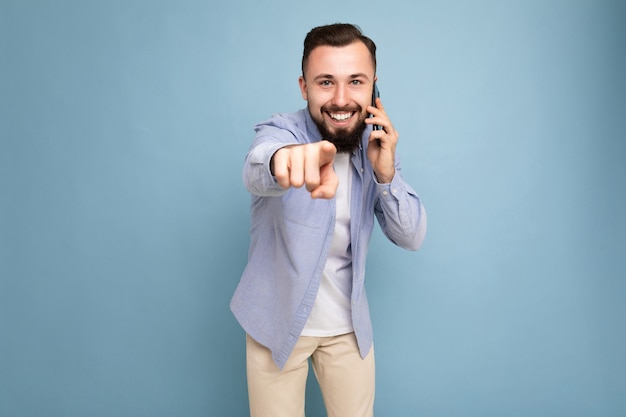 Photo prise de sourire positif beau jeune homme barbu brunet vêtu d'une chemise bleue décontractée et