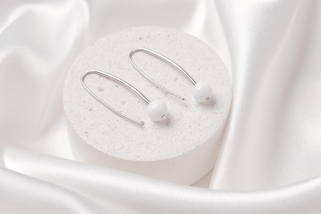 Une photo de produit de deux boucles d'oreilles en argent avec agate blanche sur un podium en béton De beaux accessoires pour femmes Un cadeau de bijoux élégant ou un cadeau pour un anniversaire ou la Saint-Valentin