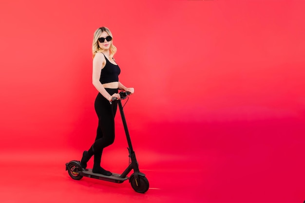 Photo de profil complète d'une femme sur un scooter électrique isolée sur fond blanc et rouge