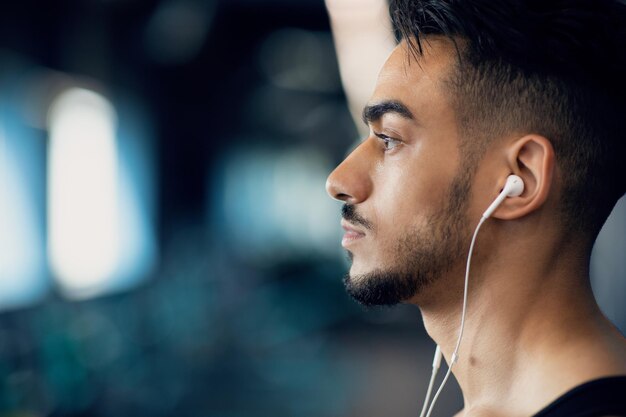 Photo de profil d'un jeune homme arabe sérieux écoutant de la musique dans des écouteurs