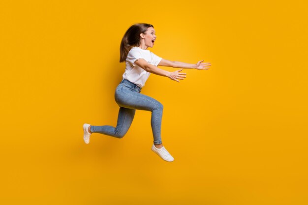 Photo de profil latéral de la taille du corps sur toute la longueur d'une jeune fille sautant en hauteur en embrassant un espace isolé sur fond de couleur jaune vif