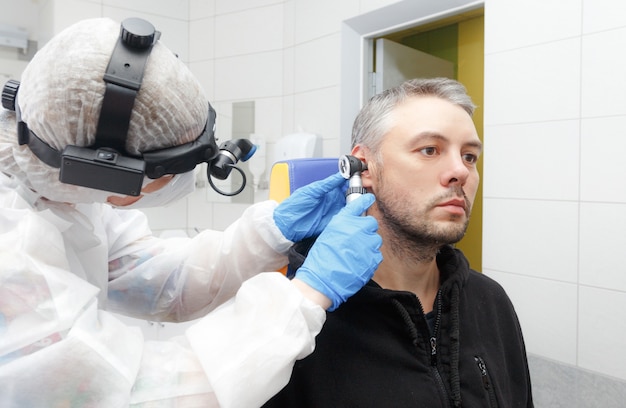 Photo de profil d'un oto-rhino-laryngologiste tenant un otoscope à l'oreille du patient, faisant un examen.