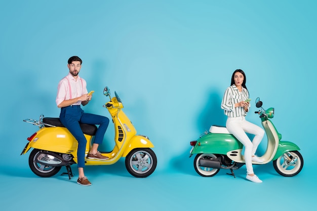 Photo de profil sur toute la longueur de la drôle de dame guy bouche ouverte au volant de deux vintage relation cyclomoteur tenir les téléphones lire vente annonce vêtements de cérémonie mur de couleur bleu