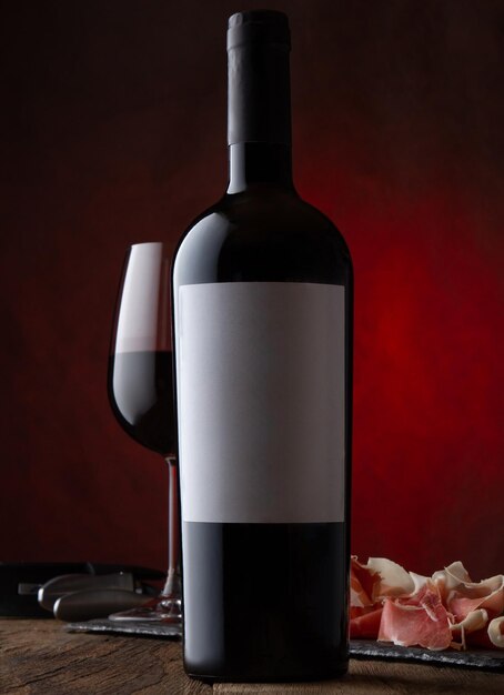 Photo une photo promotionnelle d'une bouteille de verre de vin rouge avec une étiquette vide et du jambon serrano sur du brun rouillé